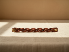 Hidden House Co. brown braided leather bracelet with a brass snap closure resting on a textured linen surface.
