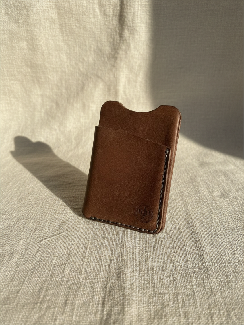 Hidden House Co. minimalist brown full-grain leather card holder with reinforced stitching on a textured fabric surface
