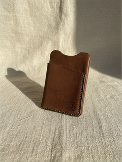 Hidden House Co. minimalist brown full-grain leather card holder with reinforced stitching on a textured fabric surface