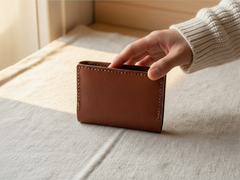 Hidden House Co. handcrafted brown leather bifold card wallet with saddle stitching held by a hand in a knit sweater.