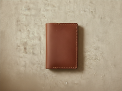 Hidden House Co. handcrafted brown leather bifold card holder wallet with visible saddle stitching on textured fabric