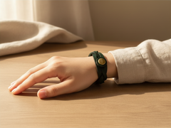 Hidden House Co. forest green braided leather wristband with an antique brass button closure worn on a wrist.