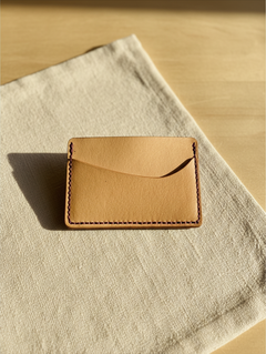 Hidden House Co. minimalist vegetable-tanned leather card holder with contrasting purple stitching on linen fabric.