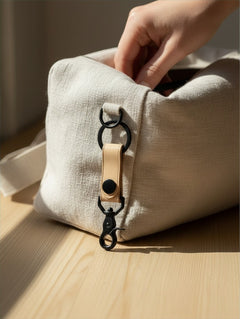 Hidden House Co. tan leather keychain with matte black metal hardware attached to a beige linen bag
