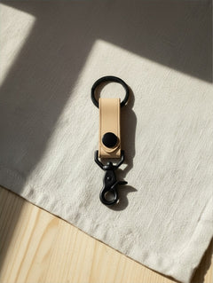 Hidden House Co. minimalist light tan vegetable-tanned leather keychain with matte black metal hardware and snap button.
