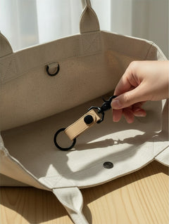 Hidden House Co. tan leather keychain with matte black metal hardware inside a beige canvas tote bag
