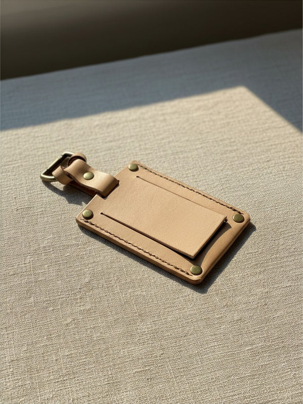 Hidden House Co. handcrafted light tan vegetable-tanned leather luggage tag with brass hardware on linen fabric.