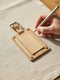 Hidden House Co. handcrafted tan vegetable-tanned leather luggage tag being filled out with a silver pen