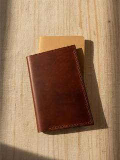 Hidden House Co. handcrafted brown leather passport and notebook cover with hand-stitched detail on a wooden surface.