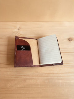Hidden House Co. brown leather passport and notebook cover with interior card slot on a wooden surface