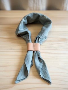 Hidden House Co. handcrafted vegetable-tanned leather scarf slide securing a sage green patterned bandana