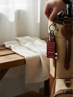 Hidden House Co. deep red handcrafted leather golf tee caddy and ball marker holder attached to a tan golf bag.