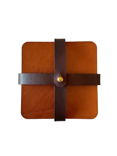 Hidden House Co. square tan leather coasters secured with a dark brown strap and brass stud closure.