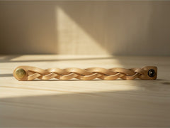 Hidden House Co. tan braided leather wristband with a brass snap closure resting on a light wooden surface.