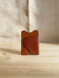 Hidden House Co. handcrafted tan leather card holder with hand-stitched detailing on a wooden surface.