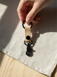 Hidden House Co. light tan vegetable-tanned leather keychain with matte black metal hardware held by a hand.