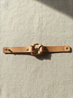 Hidden House Co. tan vegetable-tanned leather bracelet with a solid brass ring and hardware on a linen background.